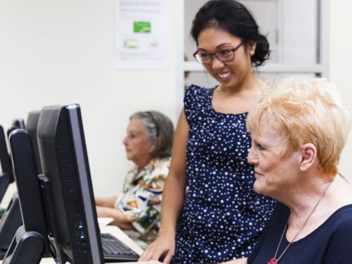 Picture of a library staff member assisting an elderly customer with a computer.